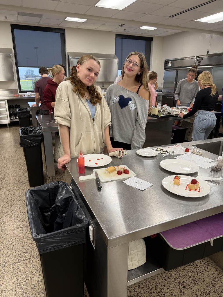 Two girls in a kitchen with a table of plates, trays, and food.