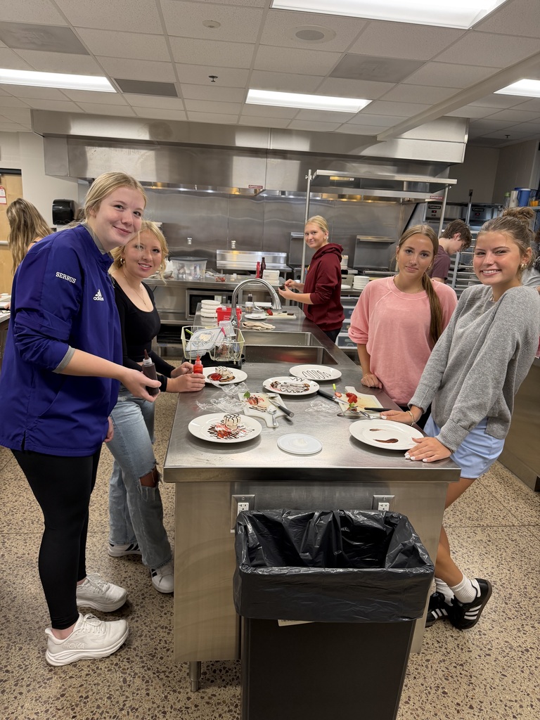 Five students stand at a kitchen counter with plates of food in progress.
