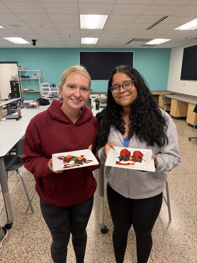 Two students in a kitchen, each holding a plate with a dessert.