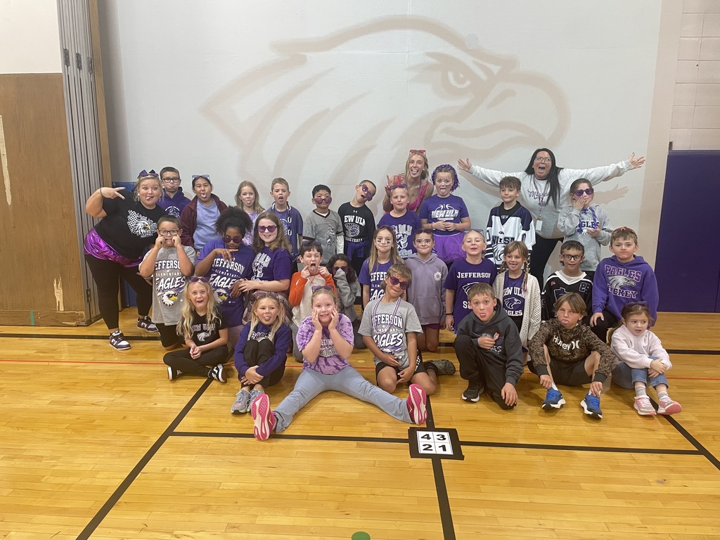 A group of children and adults in purple shirts pose for a photo in a gym.