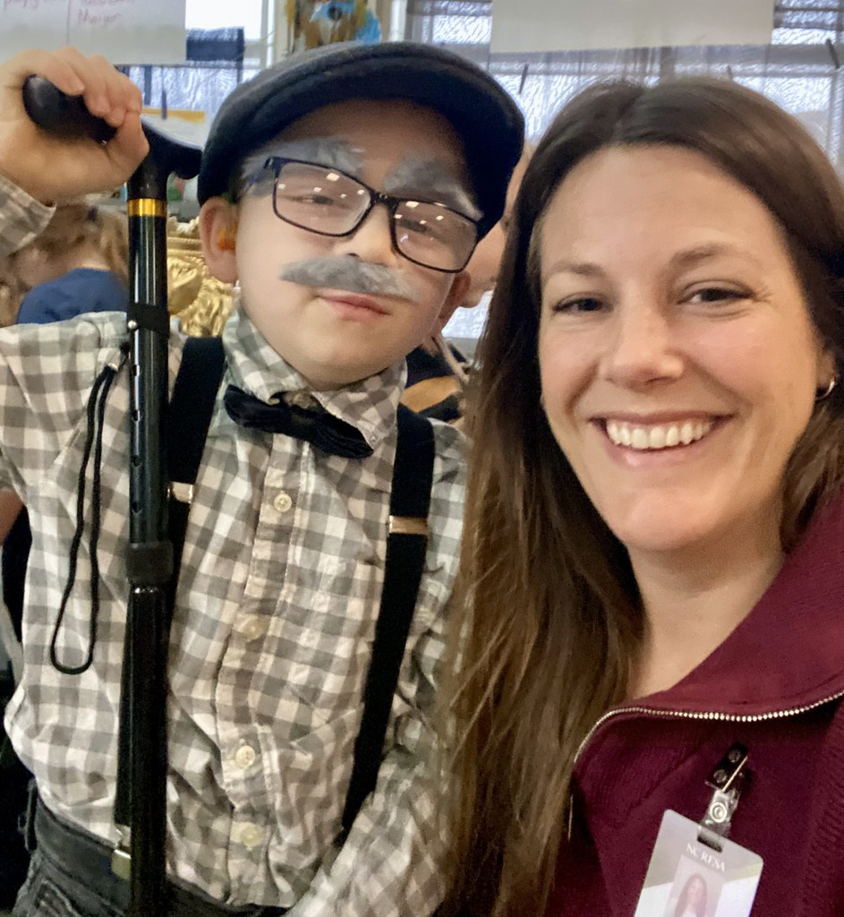 An elementary student is dressed up for the 100th day of school and poses with a teacher.