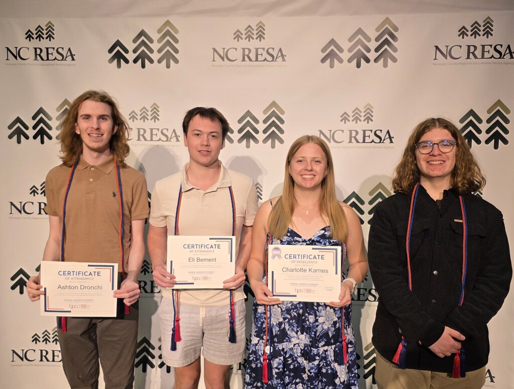 A group poses for a photo in front of an NC RESA backdrop while another person takes their picture at the event.