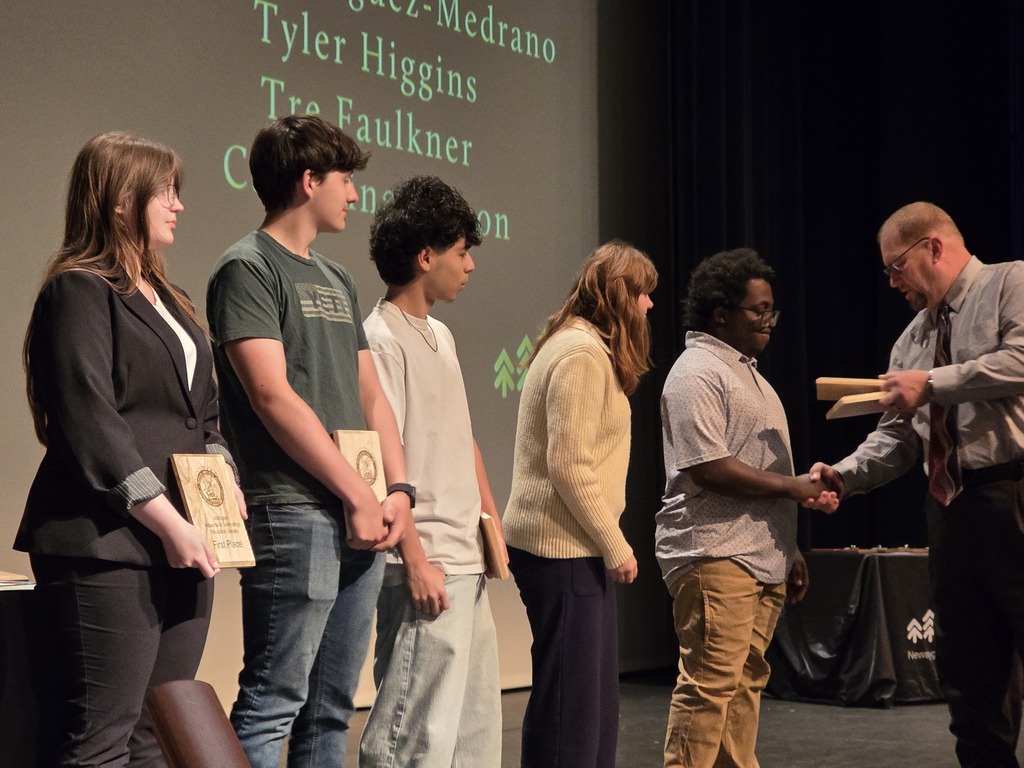 A line of students stands on stage receiving awards while shaking hands with a presenter.