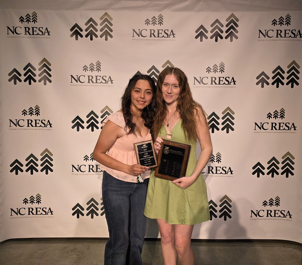 Two students pose in front of an NC RESA backdrop holding award plaques.