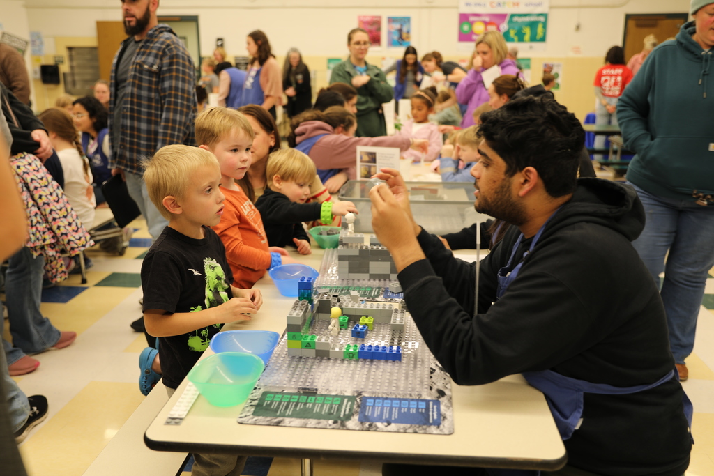 Students watching a staff member demonstrate using legos