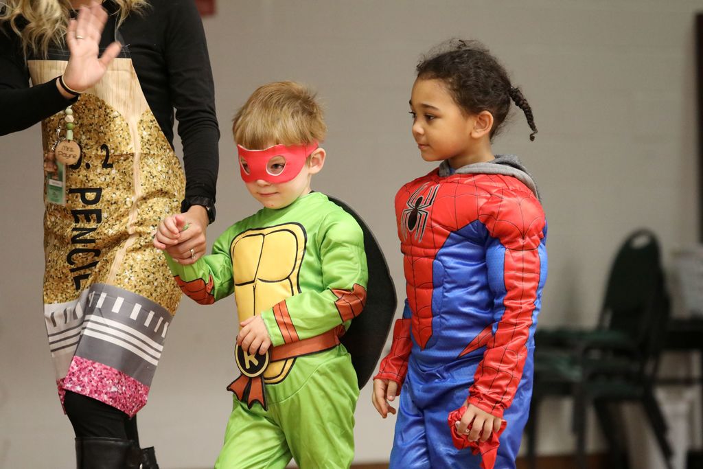 Two students walking across stage, one dress as Spider Man and one as a Ninja Turtle