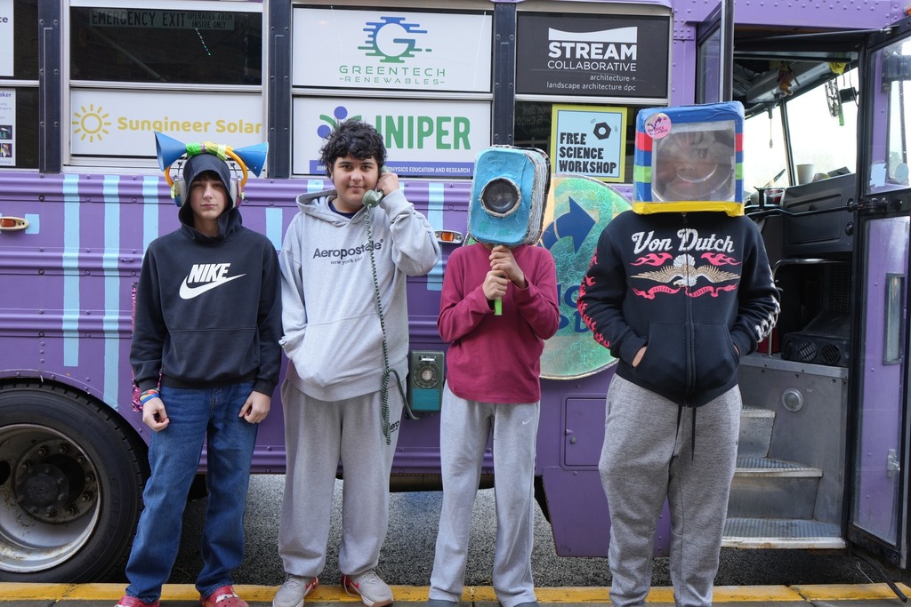four students using the equipment provided by the Physics Bus and smiling outside the bus