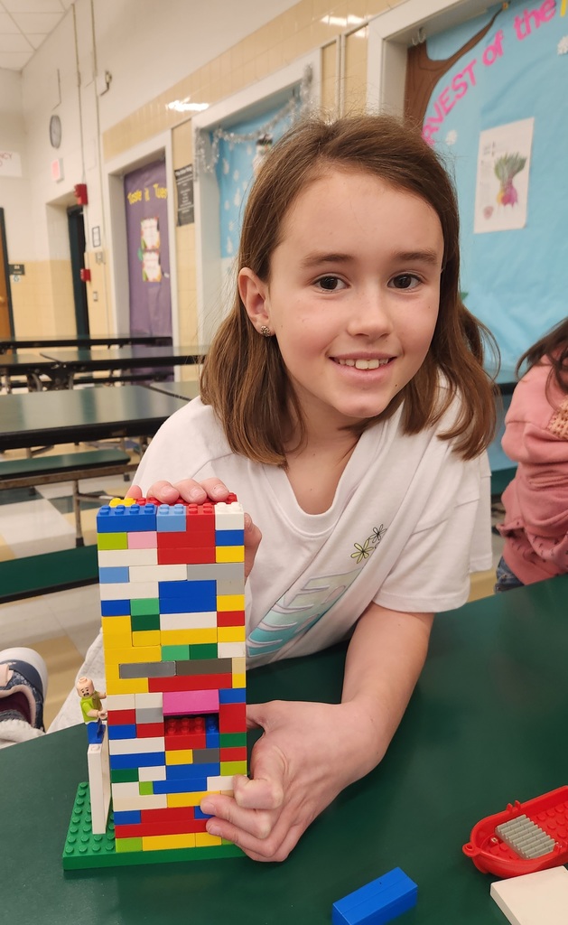 Student proudly holds a tall LEGO tower made of colorful bricks during the Green Group LEGO Enrichment activity.
