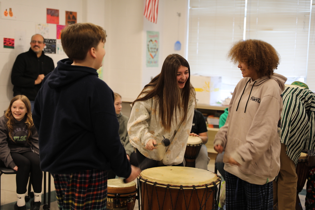 Three students laughing as they play the big drum