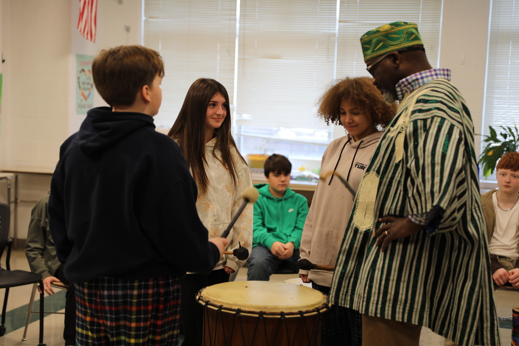 Aloja and 3 students gathered around the big drum