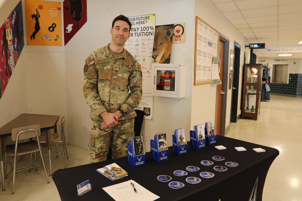 An Airforce recruiter posing for camera by his table setup