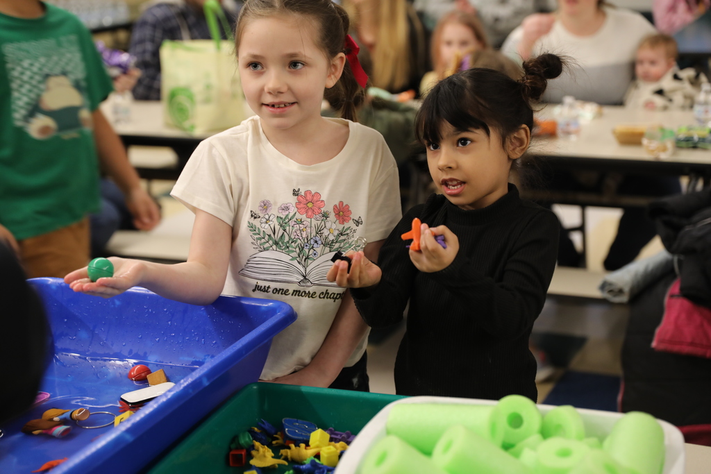 two students holding up toys they found in the water tubs