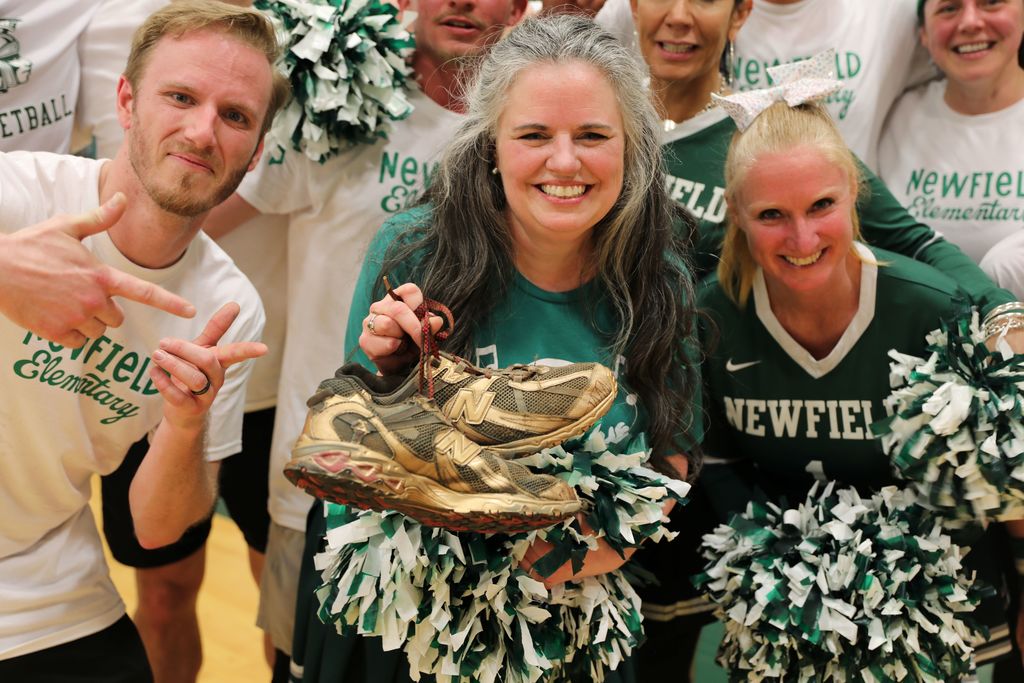 three staff holding up the golden sneakers after winning the basketball game