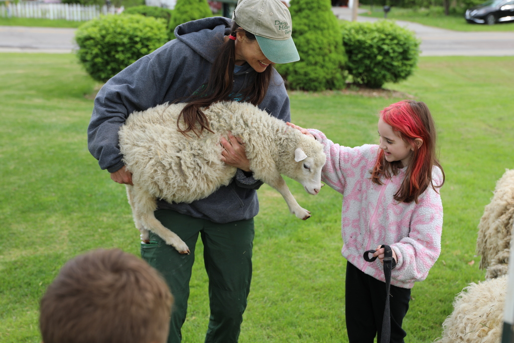 a staff member holding up a sheep so a student can pet it