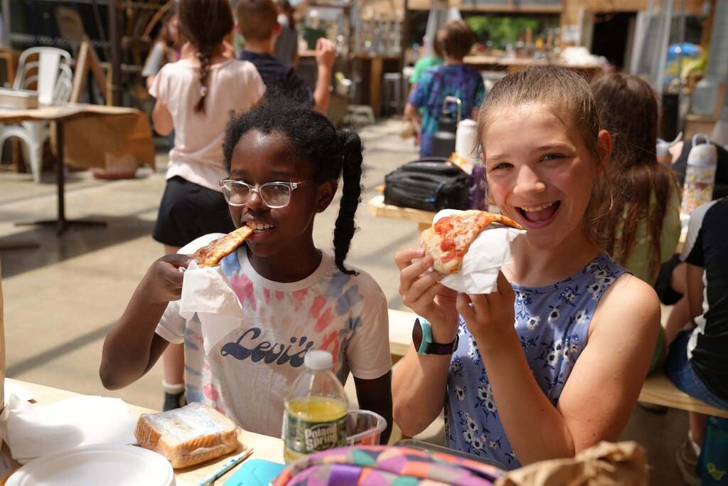 Two students enjoy slices of pizza they helped make using ingredients sourced from local farms and businesses.