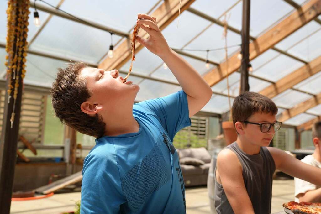 A student stretches a slice of pizza high above his head while enjoying lunch with classmates at Stone Bend Farm.