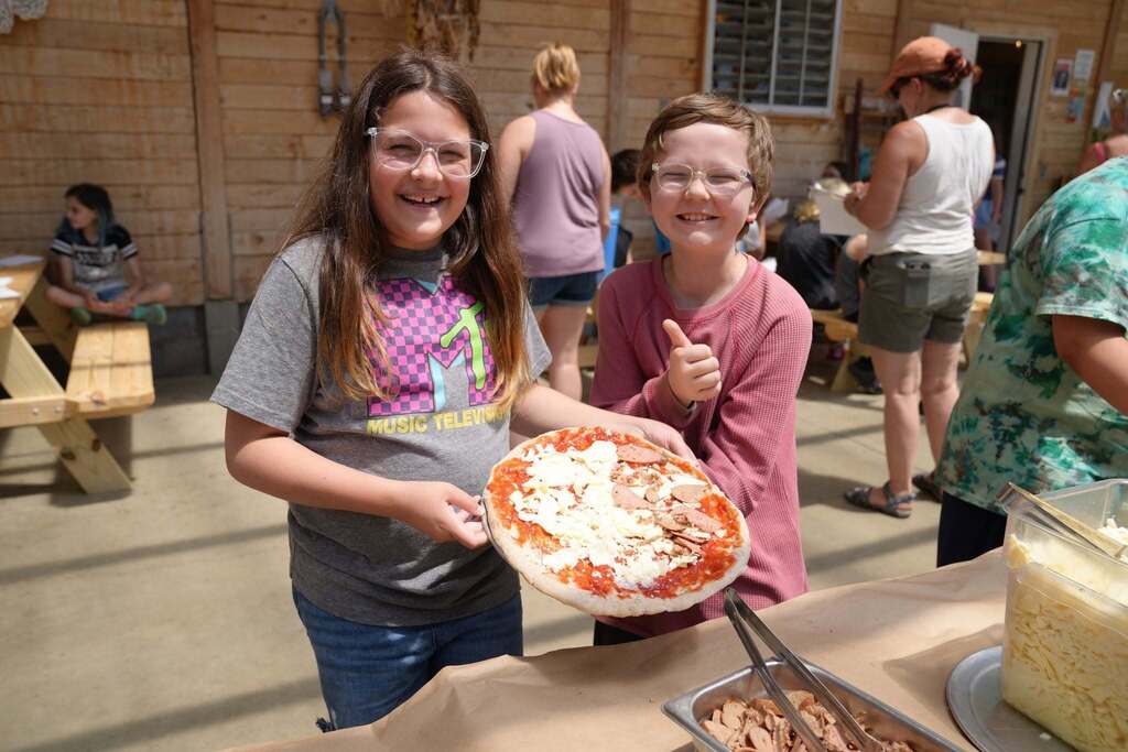 Two students proudly display a homemade pizza topped with local ingredients during the culminating farm-to-table experience at Stone Bend Farm.