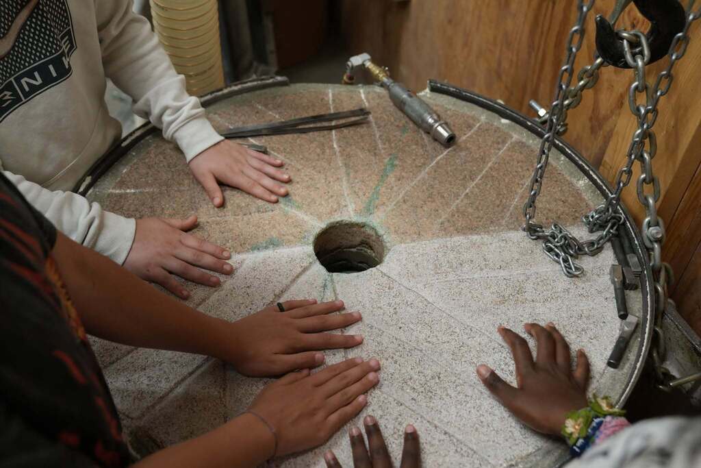 Students place their hands on a large millstone during a flour mill tour, learning how wheat is processed into flour.