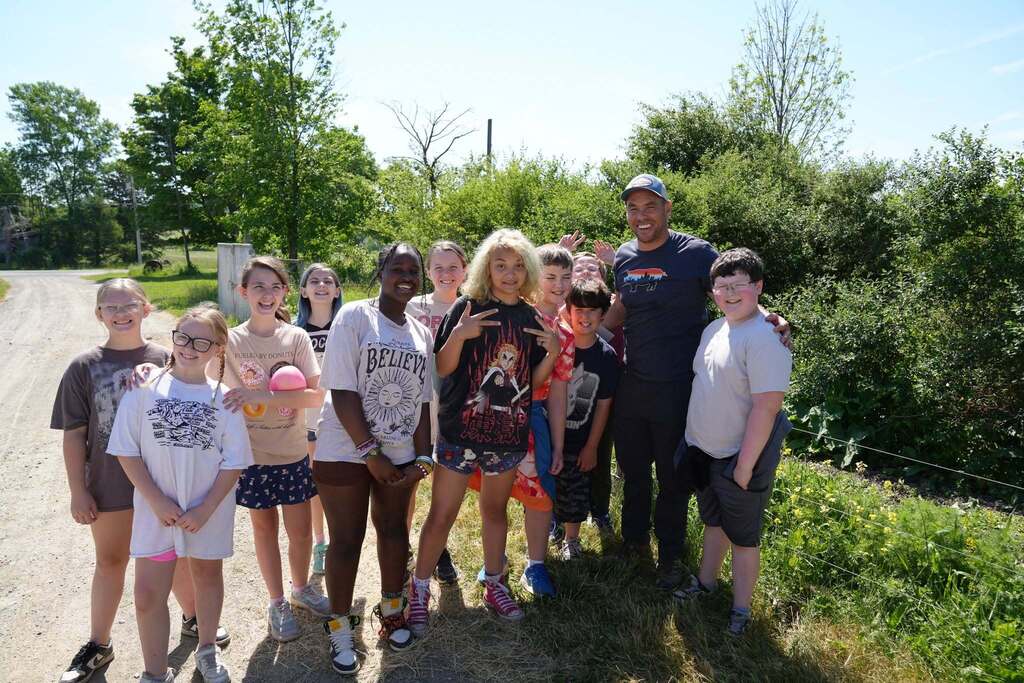 A group of fifth grade students pose with a local farmer during a farm tour as part of the Kids Discover the Farm program.