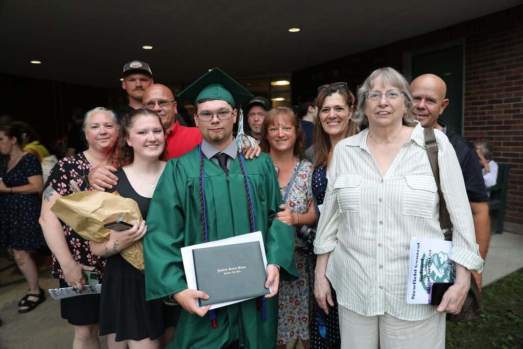 a graduate holding up his degree with his family