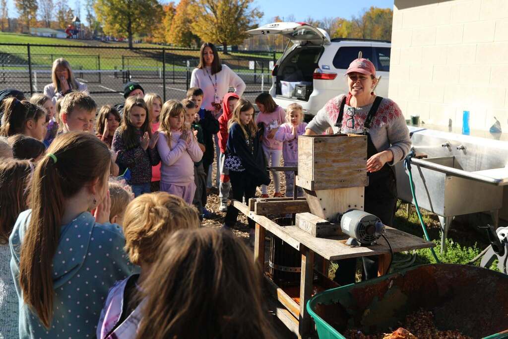 a class being shown how an apple press works