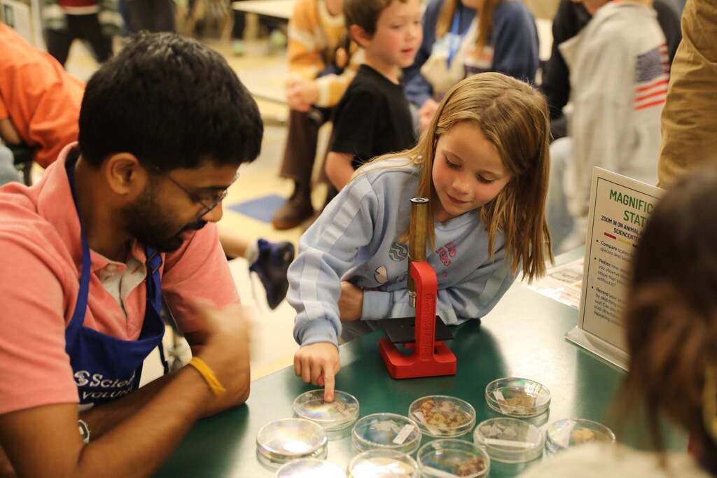 a student poiting at a petri dish to look at under a microscope