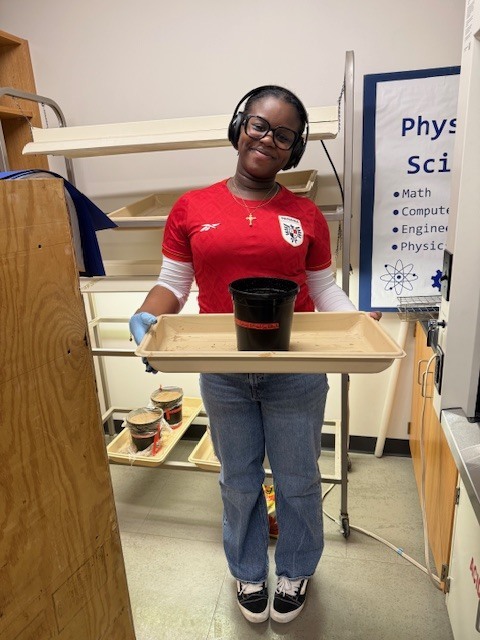 Person in red shirt and headphones holding a tray with a black cup in a room.