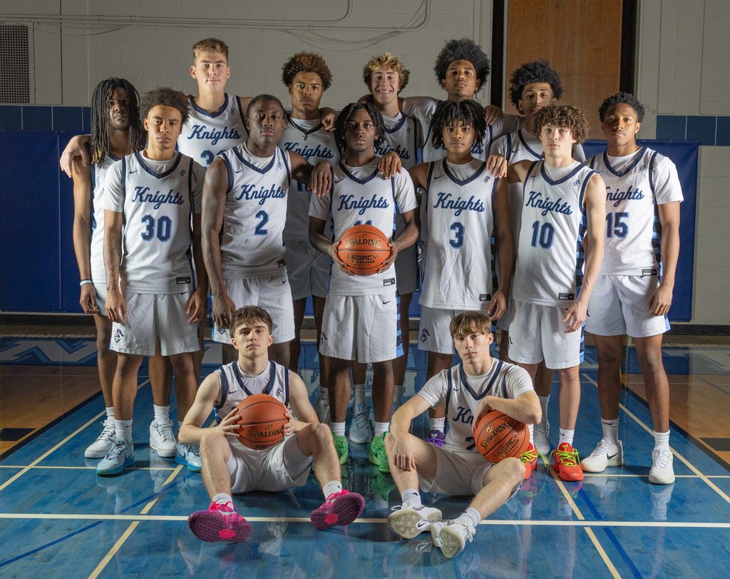 A basketball team stands on a court. Most players crouch while others stand with arms on shoulders. Jerseys have numbers and the word Knights.