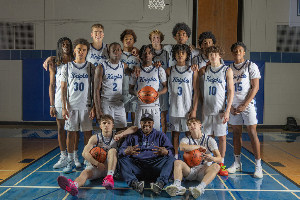 A basketball team in white uniforms poses on a basketball court with a coach in the middle.