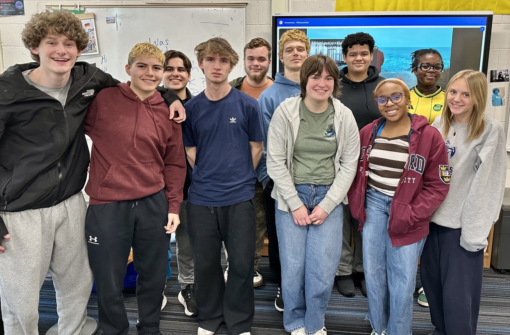A group of students, some in jackets, posing in front of a classroom screen.
