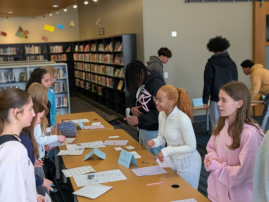 People standing around a table with papers and objects in a library with bookshelves.