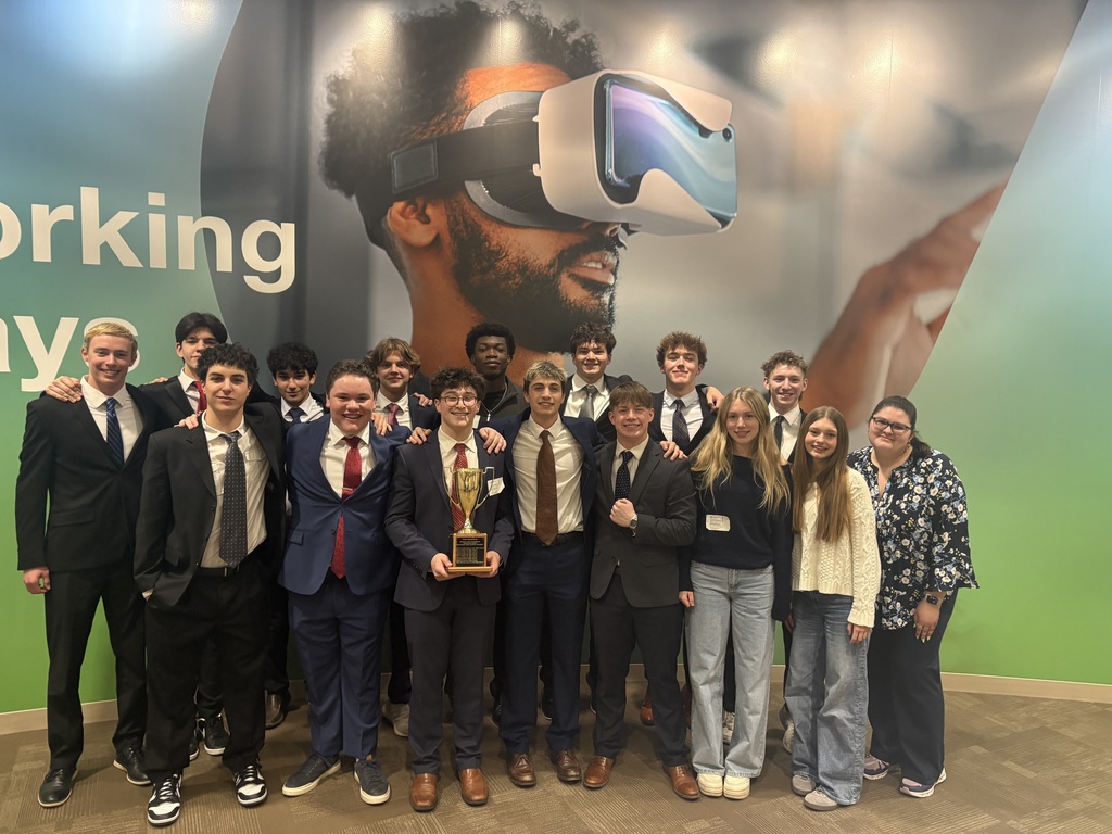 Group of people in suits, standing together in front of a large graphic, holding a trophy.