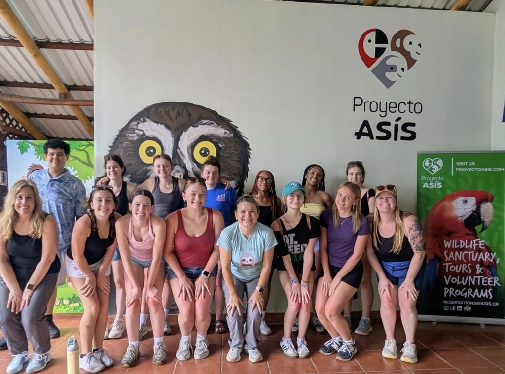 Group of adults and teens in athletic wear, posing for a photo in front of a sign.
