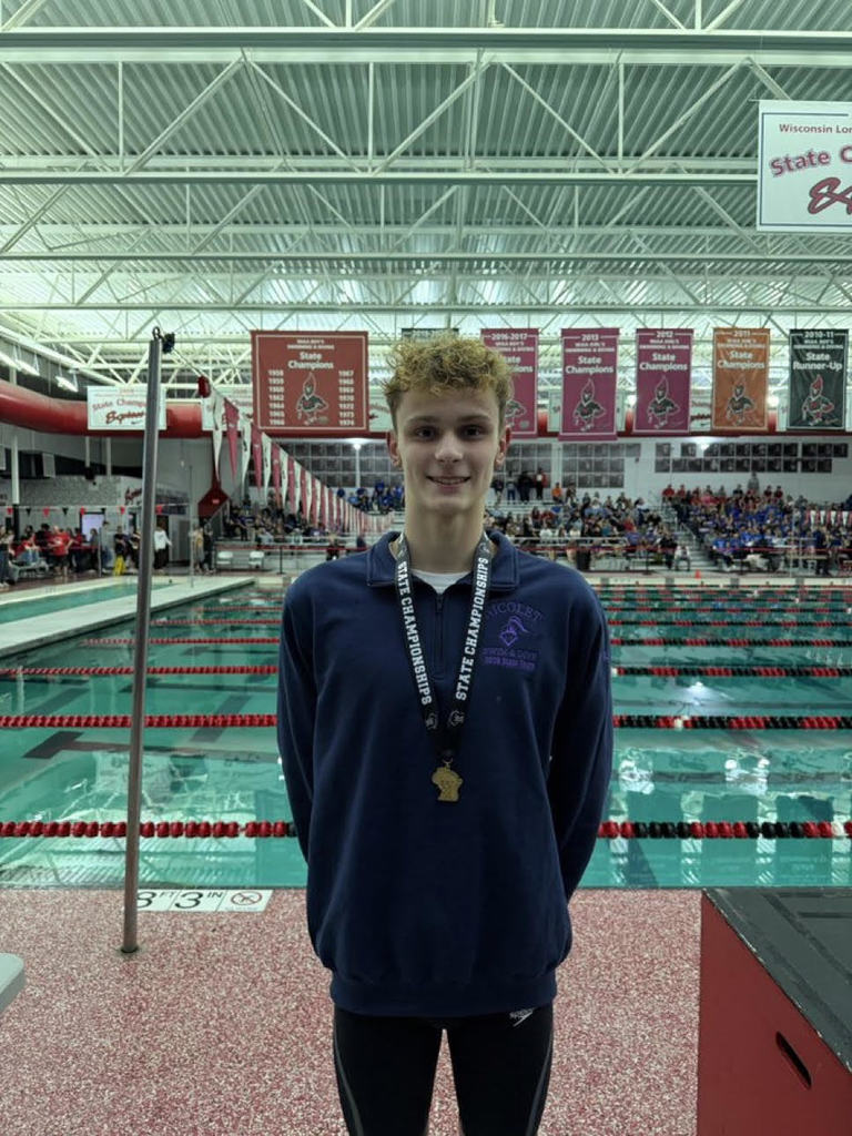 A person stands in front of an indoor pool wearing a medal around their neck.