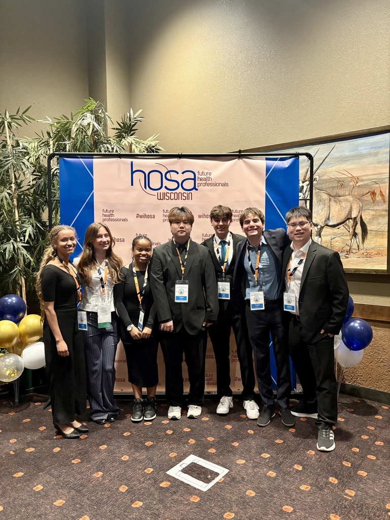 Seven people in formal wear standing in front of a banner with the words "hosa" and a giraffe image.
