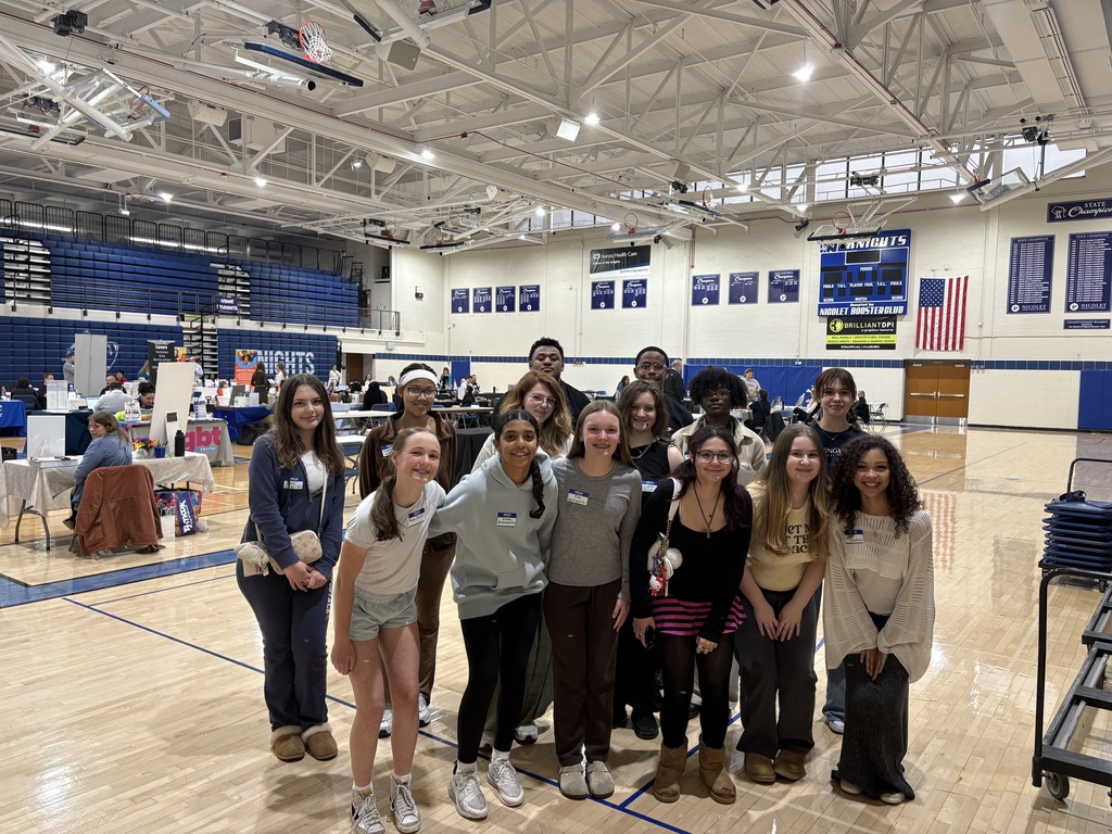 A group of people stand together on a basketball court, some in sneakers, others in boots.
