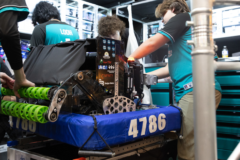 A person in a blue and black shirt works on a robot with green wheels and the number 4786.