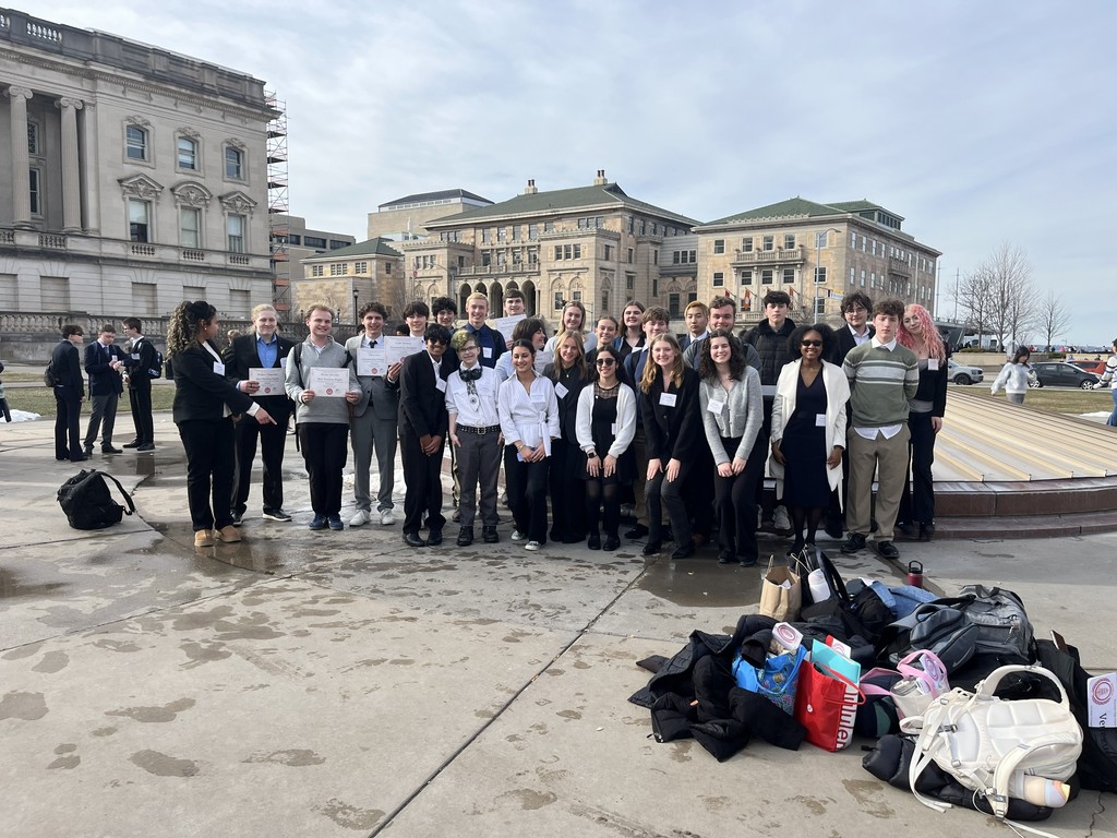 A group of people stands in a line on a sidewalk in front of a building.