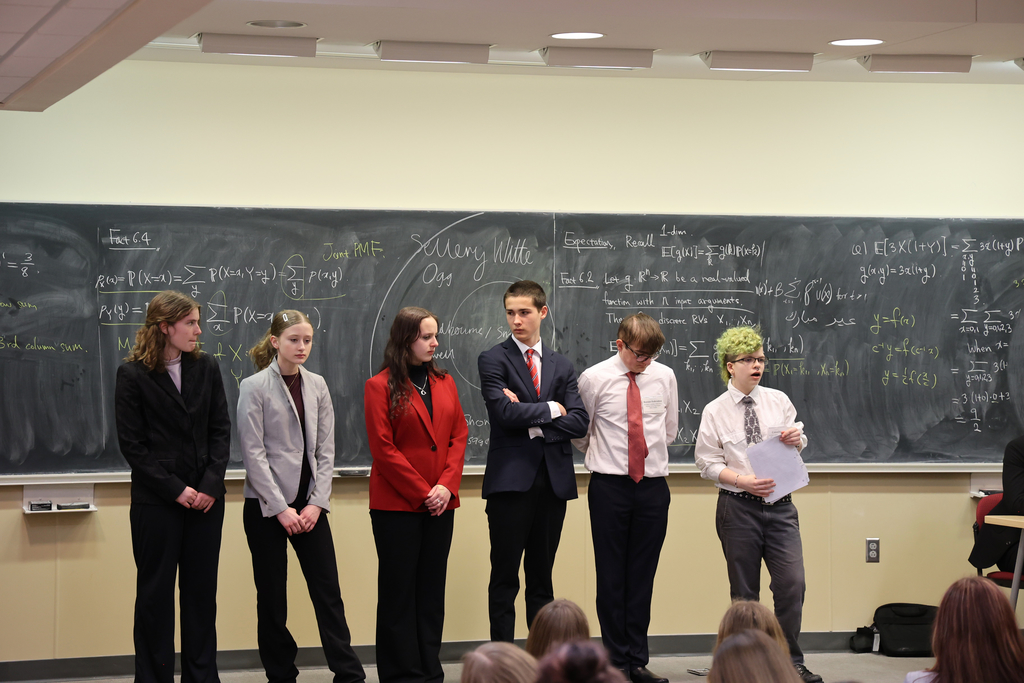 A group of people stands in a line on a sidewalk in front of a building.