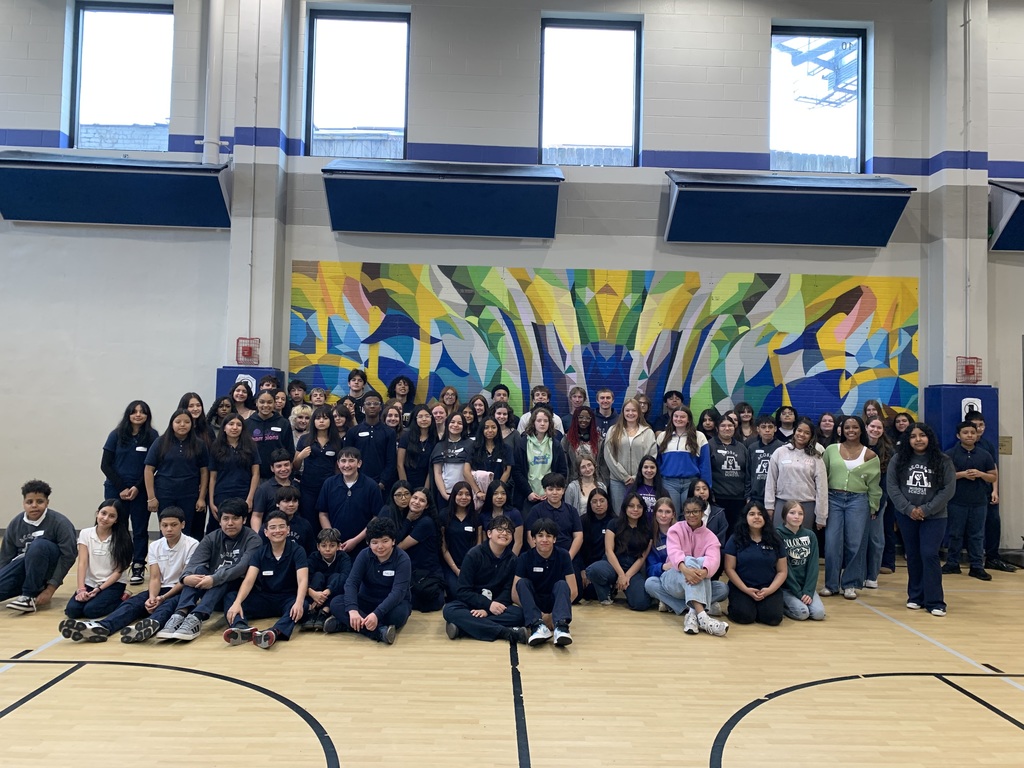 Large group of people in blue uniforms on a basketball court, a colorful mural behind them.