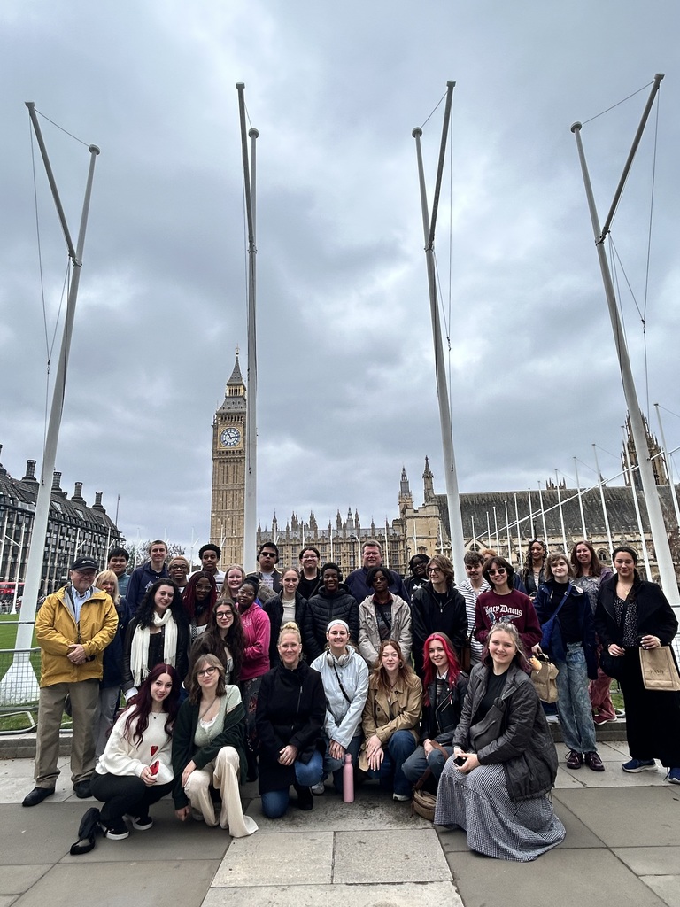 Group of people posing for a photo in front of a clock tower and buildings.