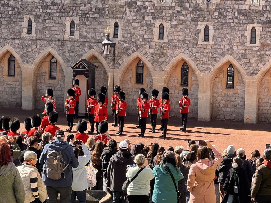 A group of people in red uniforms stands before an ancient building, with onlookers in the foreground.