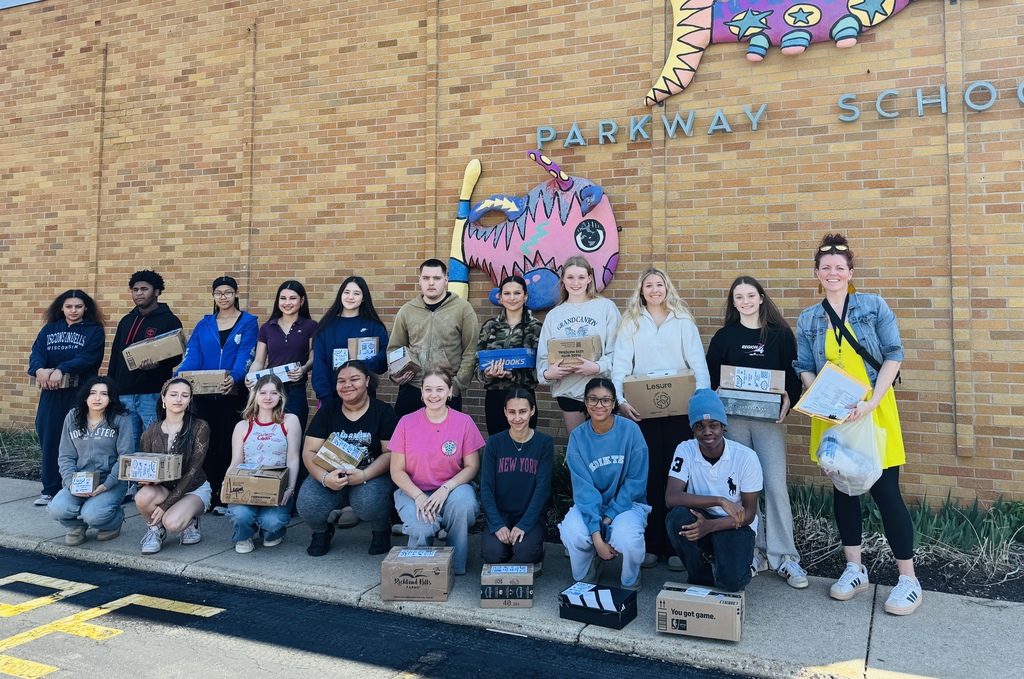 A group of people, some holding boxes, posing in front of Parkway School, with brick walls and a mural.