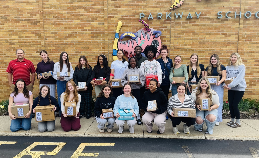 A group of people at Parkway School, holding boxes, pose for a photo in front of a brick wall.