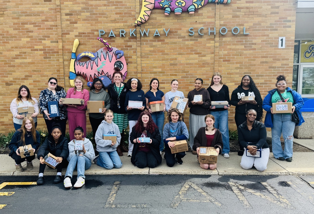 A group of people holding boxes in front of a brick building with "Parkway School" sign.