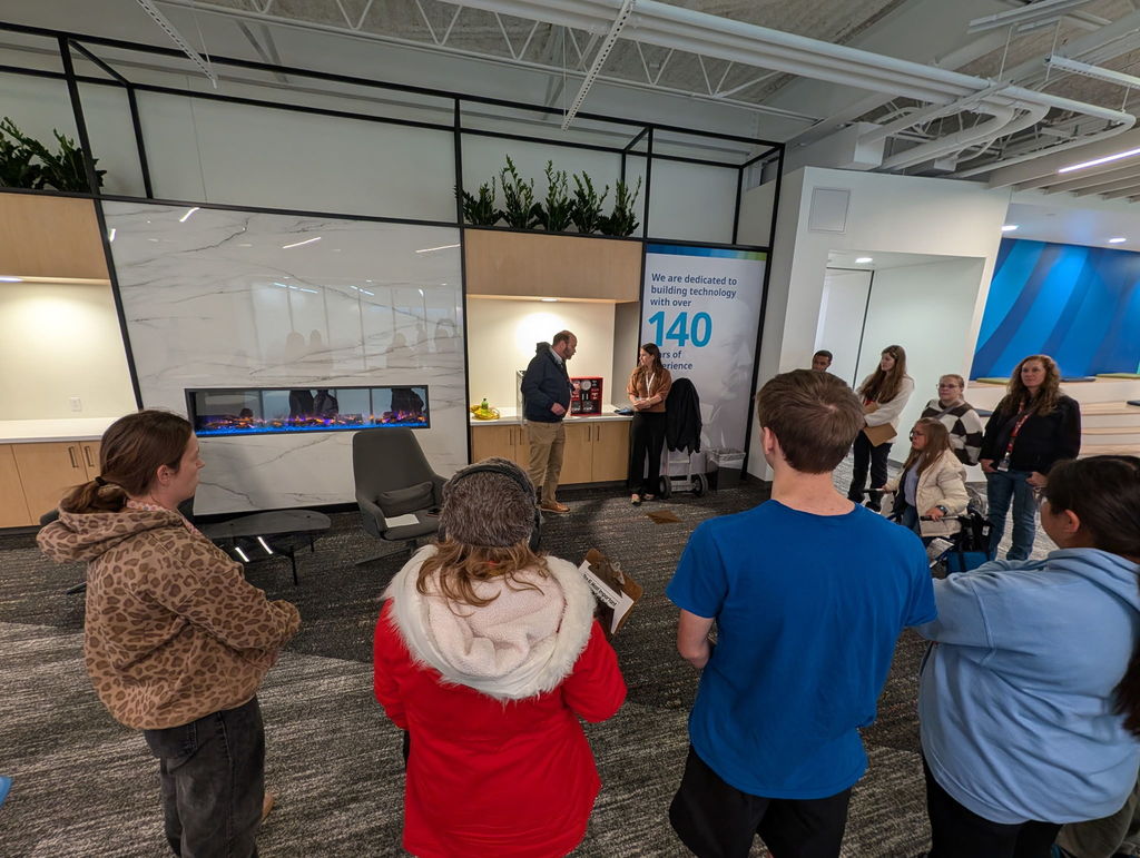 Group of people in an indoor area with a sign showing the number 140. Some wear jackets and coats.