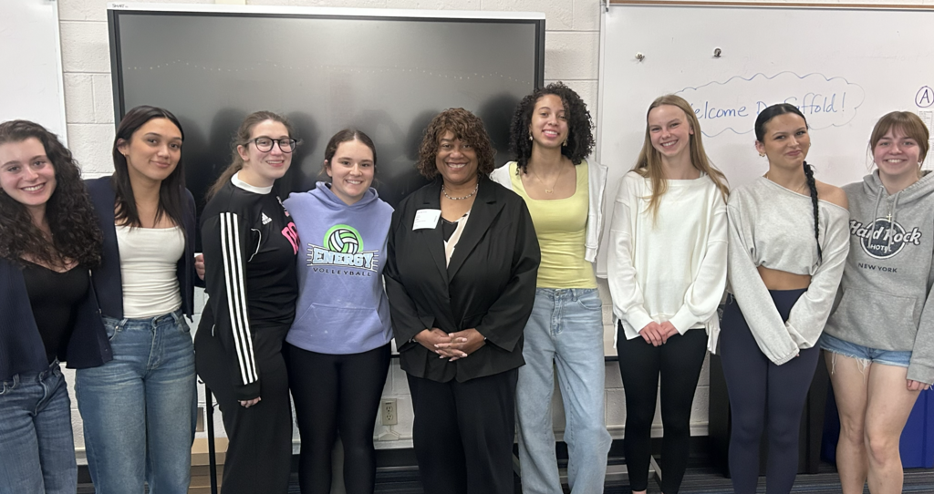 A group of women stand behind a whiteboard, smiling and posing for a photo.