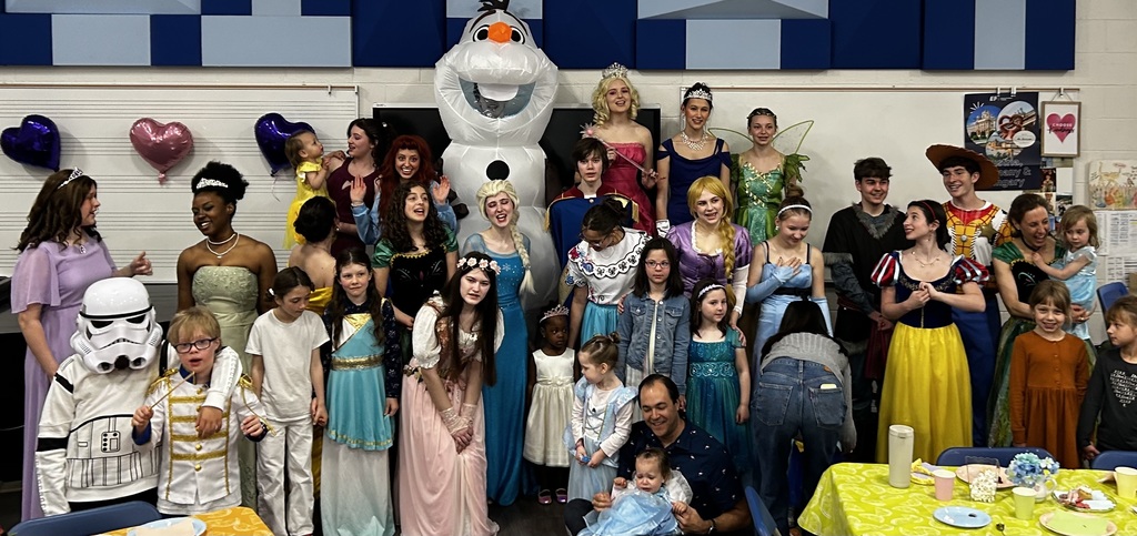 People dressed as Disney characters, including Elsa, Anna, and Stormtrooper, pose in a room with balloons and a table.
