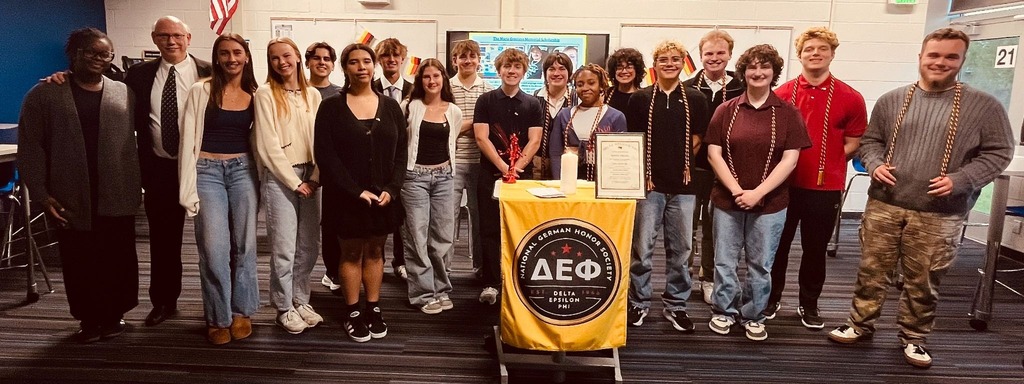 A group of students in casual attire, including jeans and sneakers, standing together in front of a podium.