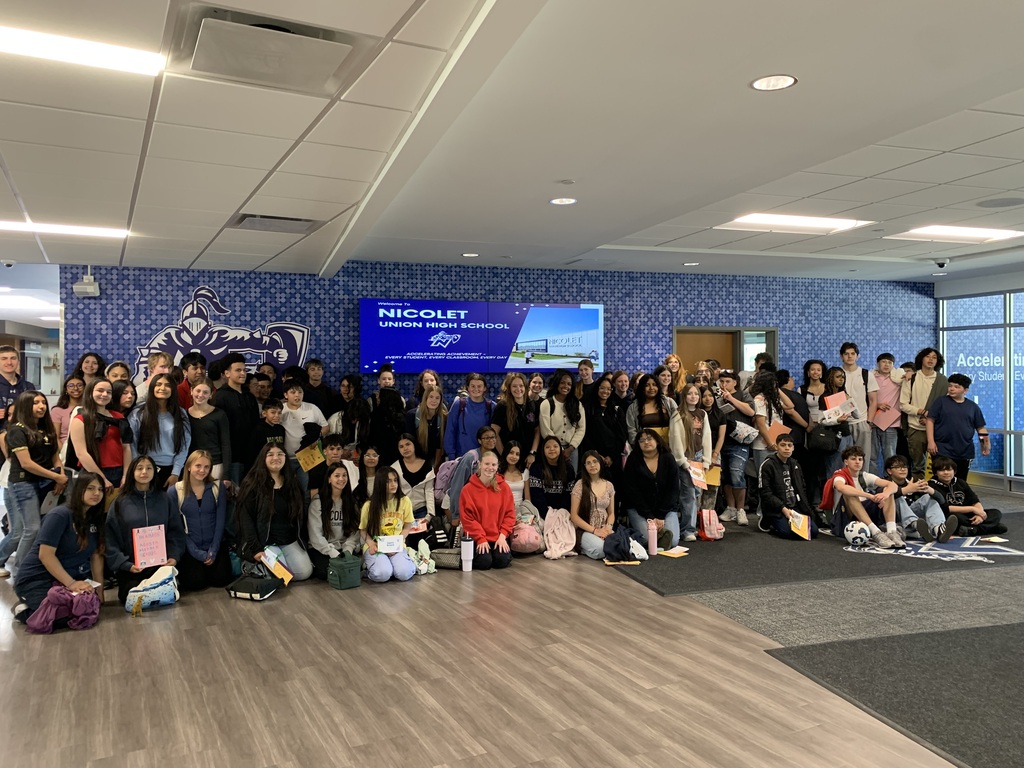A large group of people are gathered in a room with blue walls and a large screen.